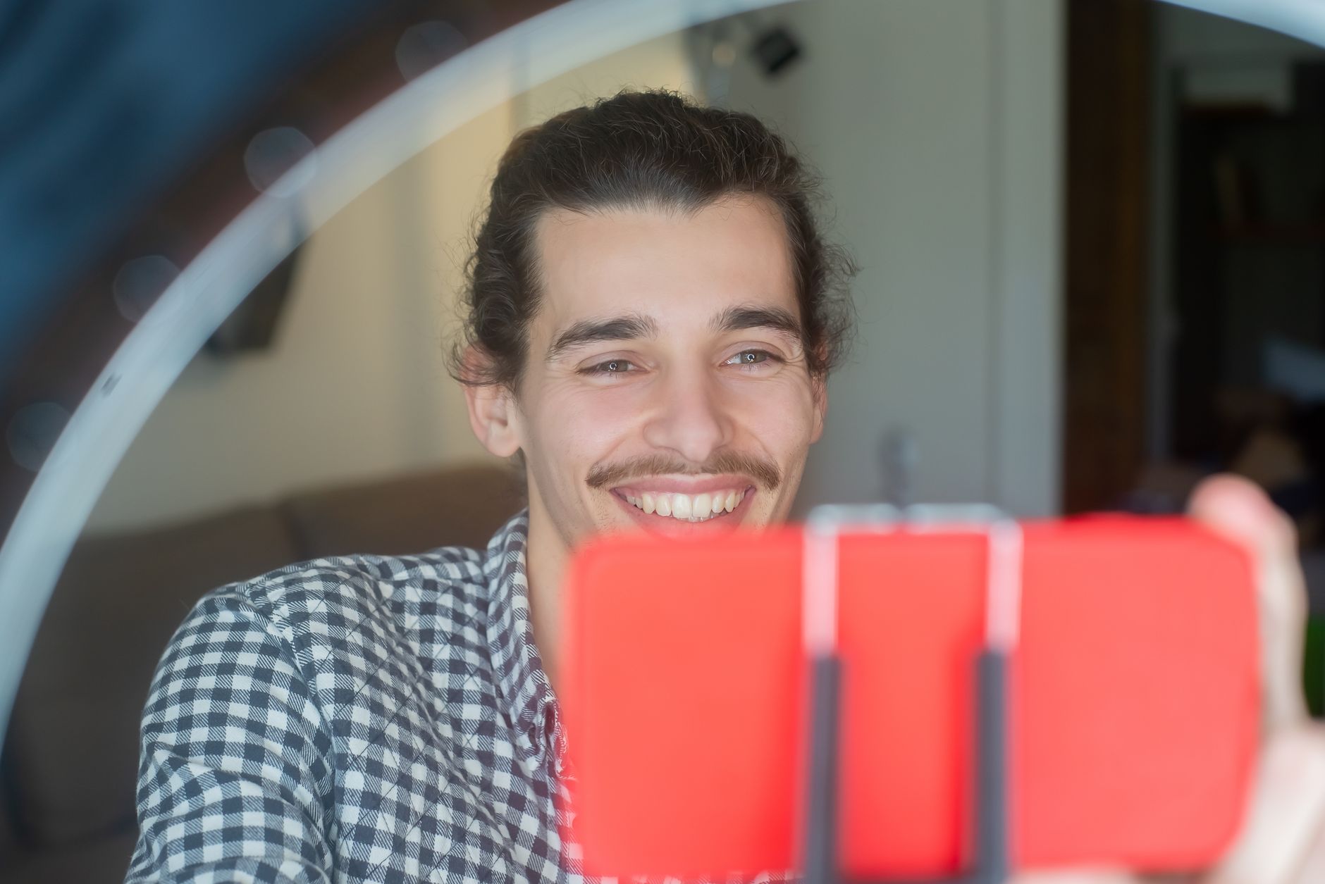 Homem sorridente a olhar para um telemóvel montado num suporte, com uma luz circular à frente.